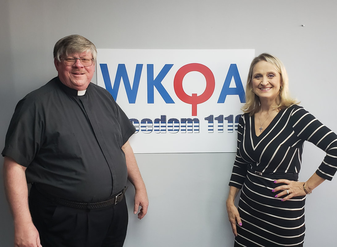 Dr. Christine Bacon and Deacon Darrell Wentworth standing near the WKQA sign in the studio.