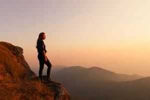 Image of woman standing atop a mountain looking into the sunset.